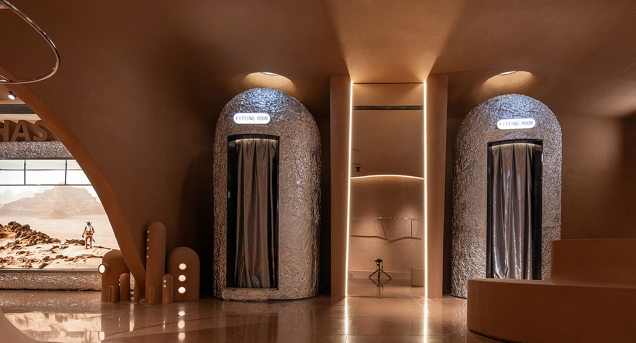 我们用道具替代功能分区,将银色隔热铝箔包裹的勘探车和胶囊状舱室,转变为服饰陈列柜及试衣间;
通过置入肌理粗粝的不规则墙体,来模拟充满原始感的星球地貌,收银台、客坐凳及灯光装置则演变为石笋,从地面及墙面自然延伸出来。