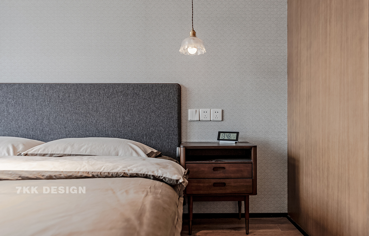 床头背景墙面选择浅灰色质感壁纸，富有肌理感。床头柜一侧墙面木饰面装饰简约而不简单，和另一侧衣柜柜体材质颜色协调一致。