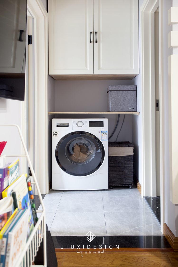 洗衣机内嵌在卫生间门一侧,旁边放置要换洗的衣物,洗衣机上部的吊柜
