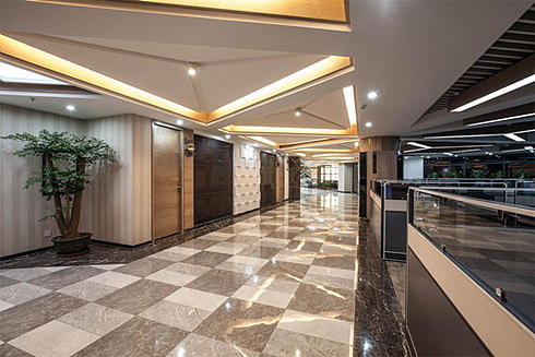 设计师对房梁进行了重新规整:放弃包梁吊顶,大胆的选择了将房梁裸露,另外安装灯槽,营造一种自然光透下来的感觉,增加了空间的感染力和饱满度,让矮房顶带来的压抑感大大削弱。“这是一种内部结构向外部结构的延伸,元素的重复和放大,让丑和美发生了奇妙的转变,房顶的线性结构和人造光源增加了空间感,如此一来平面本来就具有的大尺寸优势逐步展现出来,整个大堂具有了大空间大尺寸带来的超常感受。”