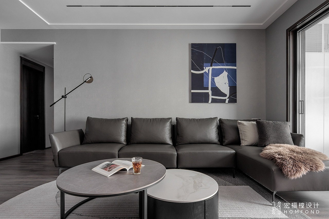 客厅为下沉式空间，从顶部到墙面再到地面，利用白色到魅影黑进行层次过渡，一幅以蓝为色块的挂画进行点缀。灰色系L型真皮沙发、大理石茶几与空间融为一体，木质地板递减冷感，低调而细腻地描绘出屋主的生活状态。加上拥有自然通透的日照光线，黑白灰空间的现代感被晕染地更加柔和。
