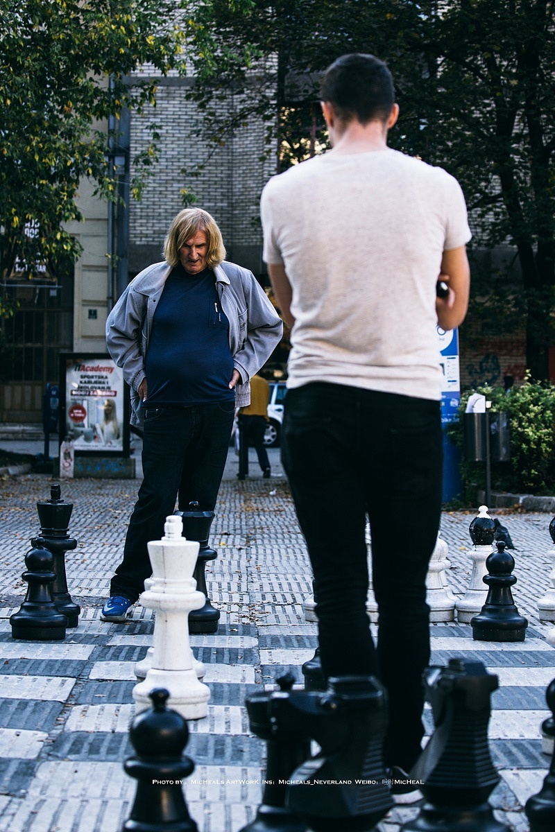 巨大的国际象棋，一个年轻人正在挑战一位看起来很有资历的大爷，而四周围满了很多类似的大爷一脸聚精会神的观察战局，场面十分紧张，战事一触即发！