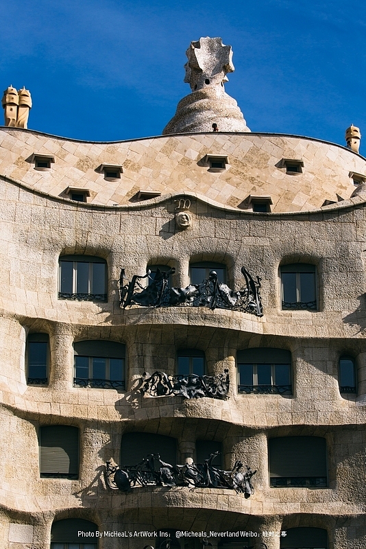 可以看到的米拉之家外立面，烟囱与楼梯间虽然立于屋顶之上，却如同蛋糕上的蜡烛，自然美观，在阁楼边沿的下方可以看到一个M字外加一朵玫瑰，这是代表了圣母玛利亚的首字母与她的象征（Our Lady of the Rosary）同时也代表了米拉夫人的名字Roser，让我们再来看看完全自由奔放的铁艺护栏吧，这些锻造工艺精妙的铁质围栏都是在高迪亲自的监督下由巴塞罗那巴迪亚兄弟工作室生产而成，几乎每一个护栏都如同艺术品一般张扬，令人感慨这位建筑大师对于每一个细节的把控与考究之情，很多人好奇一位如此偏执的建筑师，纵然有金主（没错就是你奎尔先生）的支持，却为何一再被邀请设计建造住宅，又怎么平步青云达到了如此高的地位呢？我个人认为他对于细节的认真态度，对每个建筑的全心全意，才是他成功最主要的条件。
