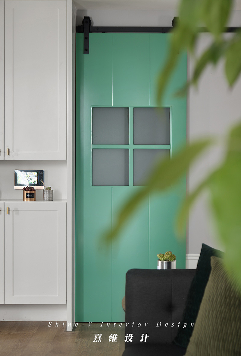 ▲入户左手边是定制的鞋柜，白色的柜体与旁边的绿色谷仓门相得益彰。公共空间以低矮的白色护墙板围绕，增加室内的美观性的同时让墙面形成层次感。
<br><br><br>客厅设置投影仪，六边形的木质组合茶几，几何形地毯与舒适的布艺沙发，一家人可以悠闲地享受家庭影音时光，客厅是能够放松下来休憩的空间。<br>