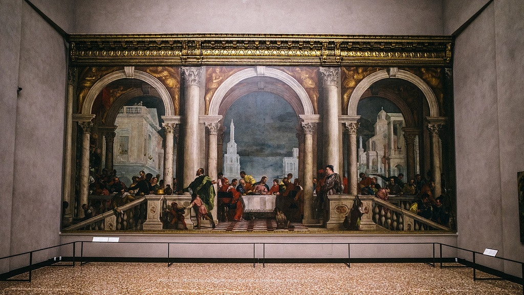 委罗内塞的《利未家的宴会》作为威尼斯画派三杰之一，这次旅程中关于他的画作见到的不多，尤其是同样作为总督府的绘制者，他的画作被丁托列托的两幅巨作抢尽了风头……Anyway，保罗-委罗内塞（Paolo Veronese，1528-1588）是提香的弟子，其浓郁的世俗风格充满了生活的琐碎与情趣，搭配丰富的色彩与人物表情的自然张弛，是更具有装饰性的一种风格模式，也就是巴洛克的雏形。这幅巨大的画作原本名为西门家的宴会，然而因耶稣参与其中，并牵扯到圣人，画中的侏儒小丑，醉汉，狗，猴子，甚至流着鼻血的仆人，过分世俗，被指责触犯了宗教法令，甚至被传唤庭审。这段庭审是有被文字记录下来的，看过之后会佩服这位画家对于表达自由的向往与执着，而巧妙的将名字换为凡夫俗子家的家宴也避开了宗教中的场景，令其躲过了这场风波。约束创作的永远是令人不齿的条框规矩，这些压抑的东西何时能被抛去，创作更加自由时，才会有更多美的作品被释放出来，对，我就是映射了，喵的创作者该被谩骂与职责么？分明是制度的问题，有本事去找制定制度的人去骂，没本事就憋着。