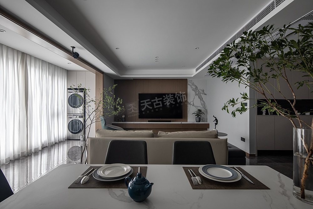 客厅打通了阳台,既增加了采光,又让整个横厅简约大方。以沙发做隔断,背后留出3米的距离让餐厅与走道完美的融入其中。电视背景墙运用到木饰面与石材的组合,生成强烈的层次感,同时在下面增设收纳地台,兼顾储物功能。客厅吊顶里隐藏的无主灯灯光顺着墙面洒下来,光影与木质、石材交错共生,沉浸式的氛围感铺面而来。