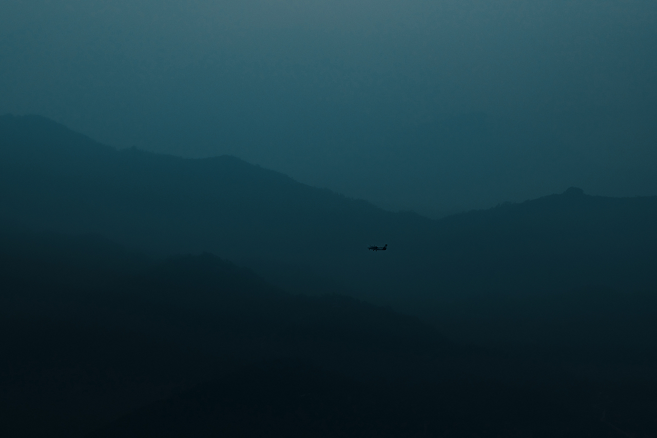 一架飞机孤独地穿越群山。晨雾漫过山崖,远处草甸深厚,河流浓稠。