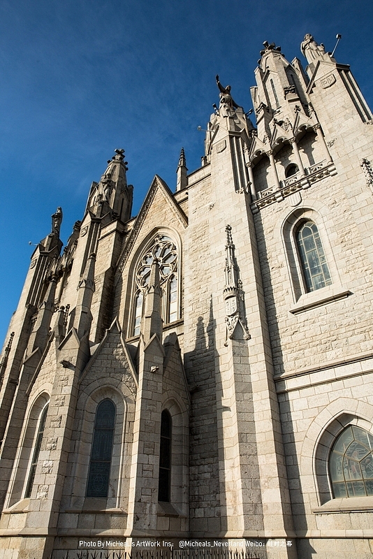 这座教堂分为两部分，上层是新哥特的风格，下层则有些加泰罗尼亚当地特色的外观风格，设计者为西班牙建筑师萨尼耶父子共同完成，前期由父恩里克-萨尼耶（Enric Sagnier）负责，而最终完成则是靠后期的子约瑟夫-玛利亚-萨尼耶（Josep Maria Sagnier）从最初1902年至最终完成时以是1961年。图中的便是上层建筑的外观，立面干净利索，且石制偏白，大概因为此教堂的构想源于巴黎的那座圣心圣殿吧（最初的教堂篇有提过那座教堂就不熬述了）整体风格很漂亮，只是这个山头来一趟相对比较远，在加泰罗尼亚广场旁坐公交车即可到达，班次较少结束运营时间也很早，所以很多人推荐自驾……Emmmm不了吧不喜欢开单行道太多的城市Orz~