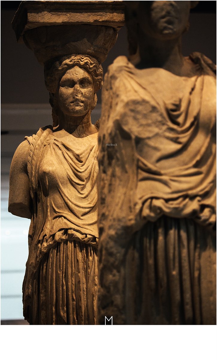 030:在博物馆中，收藏的是卫城一些未被窃走的文物，其中当然就有那五根女神柱的本体。虽然应用了爱奥尼克立柱的模式，却完美的将柱体本身雕刻成了女神的模样。虽然这种创新的方法颇为理想化，但是它在当时的古希腊是需要面对一些技术难关的，最为困难的，就是根据完美人体比例来雕刻女神的话，脖子位置的柱身过于细长会无法做到柱子承重的效果，而当时的大师们在女神的头发后颈位置添加了披肩辫子，完美的解决了这个问题又增加了美感。令人称赞古人对于数学几何物理这些科学的掌握程度，灵活运用，以及他们对于美的执着向往。