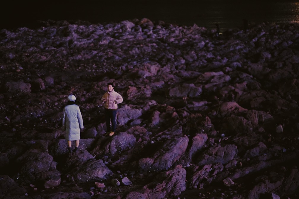 栈桥的夜晚,一对情侣站在海边的岩石上面。