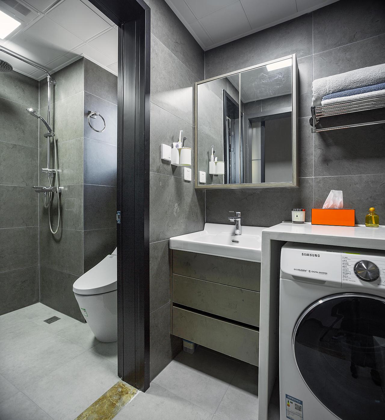 卫生间干湿分离的设计，选择灰色大理石砖，白色台盆柜与侧面台面相连接，嵌入式洗衣机，延长台面的长度。
亮橙色的纸巾盒再次出现，卫生间中一抹亮色，可见主人真的是很喜欢，台面上摆放着香薰等精致小物，简约高级。