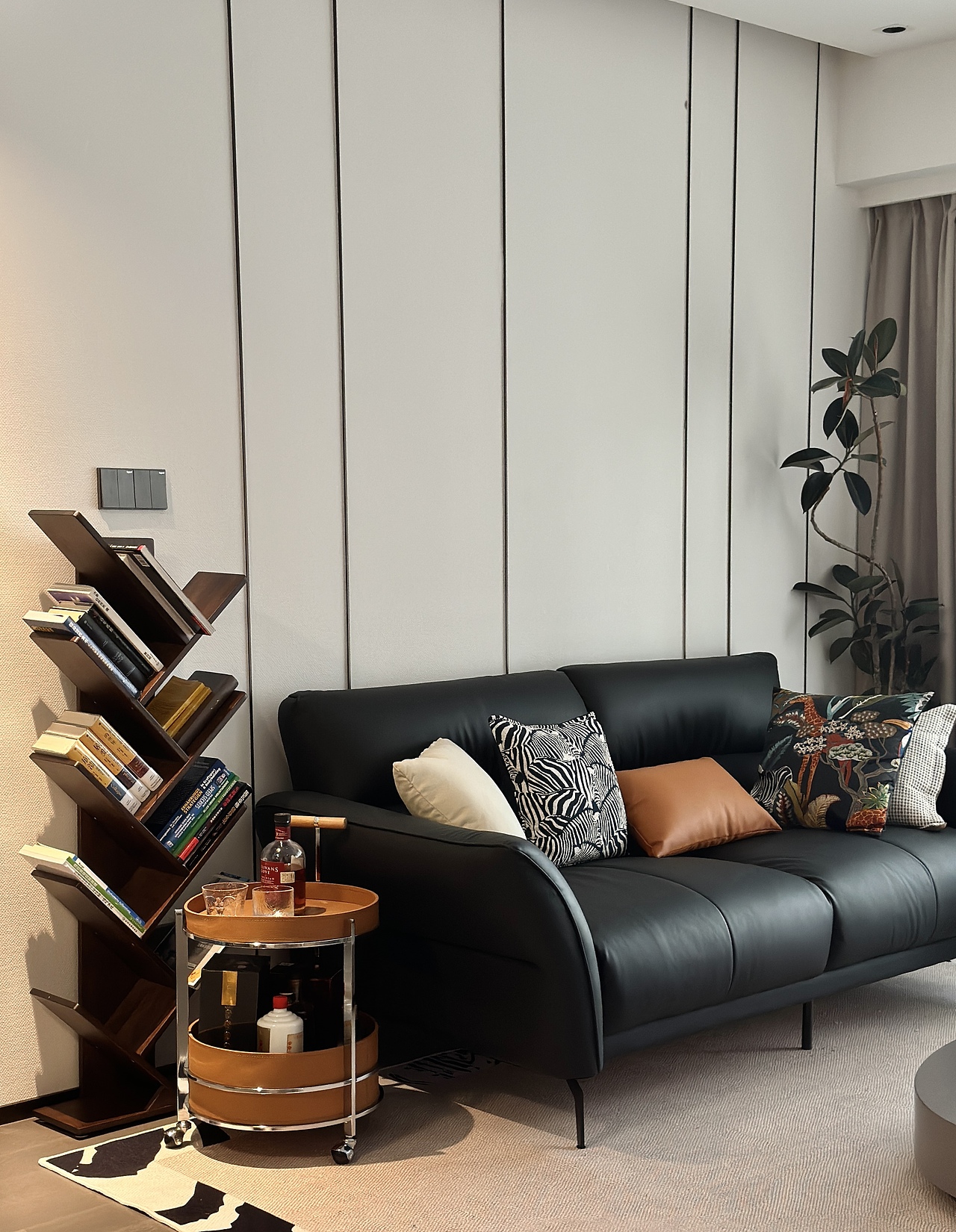 狭长客厅,正对三个门洞(卧室、衣帽间、厨房),采用黑色双人沙发加重空间分量,搭配架空茶几、高挑的书架以及绿植,破客厅的沉闷感觉。