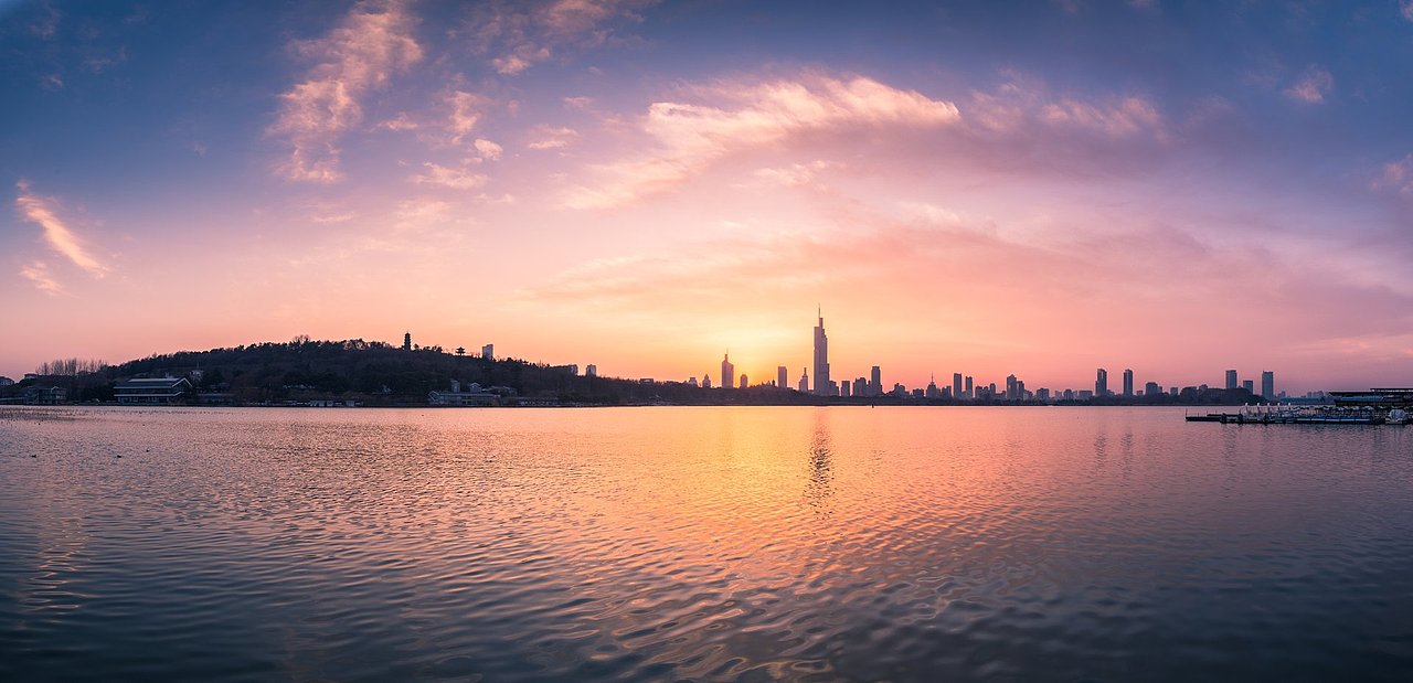 从玄武湖边远望即将落入地平线之下的夕阳蓝天白云下南京城东连绵的