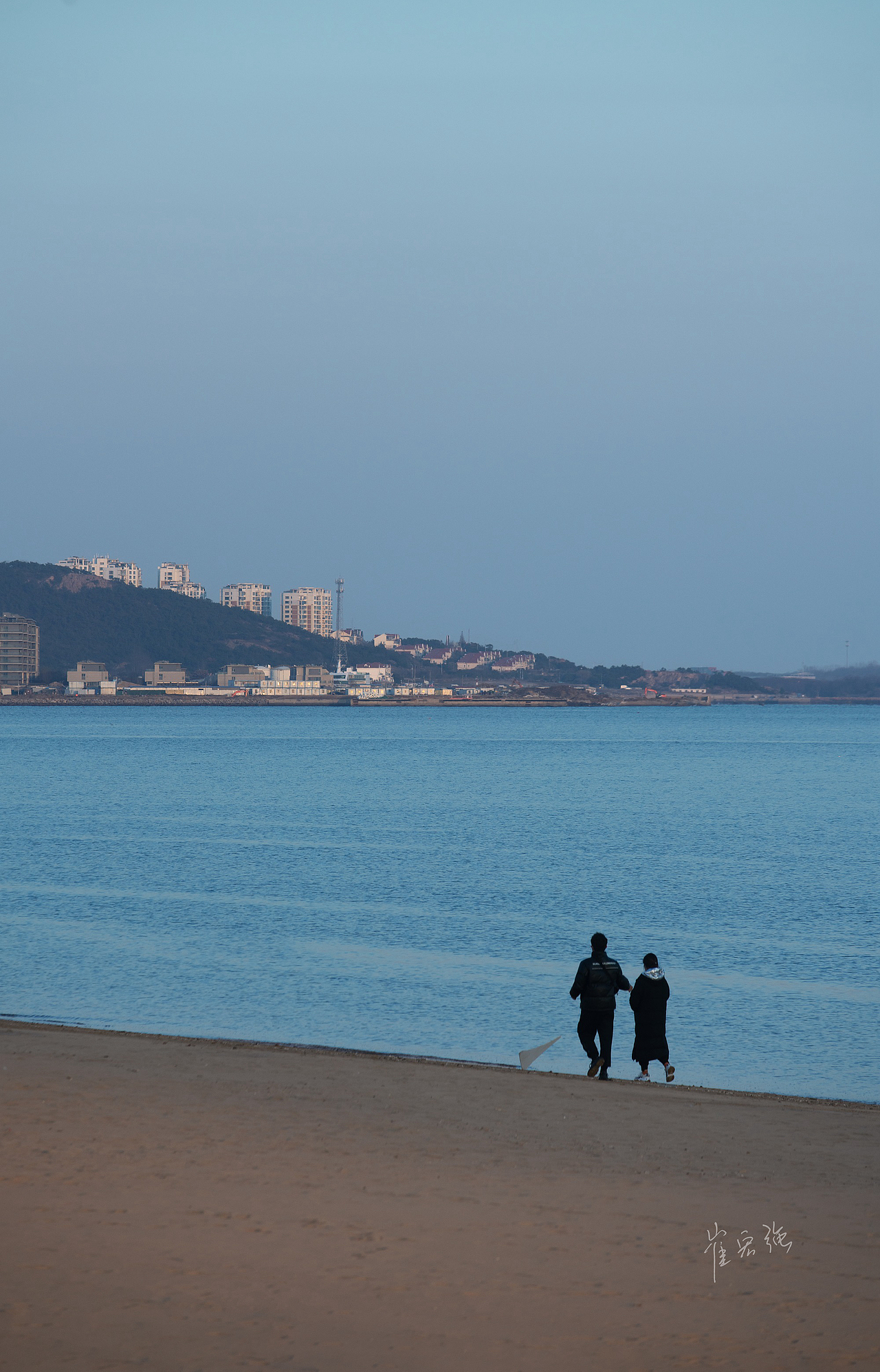 阴沉的天空下,一对情侣沿海边漫步私语。