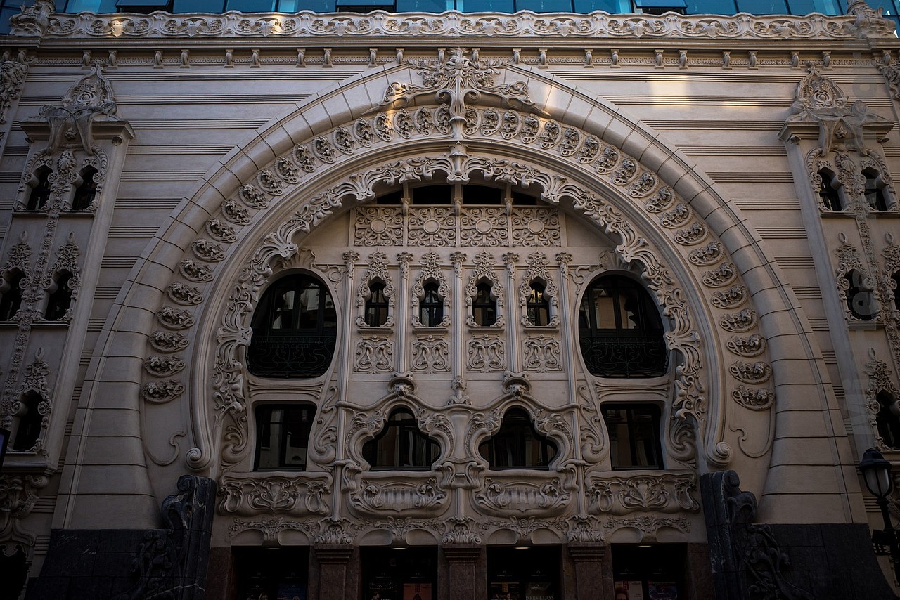 在毕尔巴鄂较为狭窄的现代区域街道中,有一个极为令人感慨的剧院立面早早就吸引了我的注意,毫不犹豫冲了过来,非常之满意!被称为香榭丽舍剧院(El Teatro Campos Elíseos)与法国那条街道可能关系不大(也有可能是街道太有名这个词儿就显得很高级?) 无论如何吧。它修建于1902年,由当地建筑师阿尔弗雷多-阿斯巴尔(Alfredo Acebal)负责建设,法国建筑师让-巴蒂斯特-达洛基(Jean Batiste Darroquy)负责立面设计的典型“新艺术运动”风格剧院十分抢眼且美观,装饰性极强的拱形外廊搭配精美的弧形浮雕,让观众入口变得十分隆重,进入剧院的体感拉满。又很聪明的分开了工作人员入口和别的通道,让他们弱化了存在感,无奈当日没什么演出,不然我一定得看上那么一场体验一下Orz!