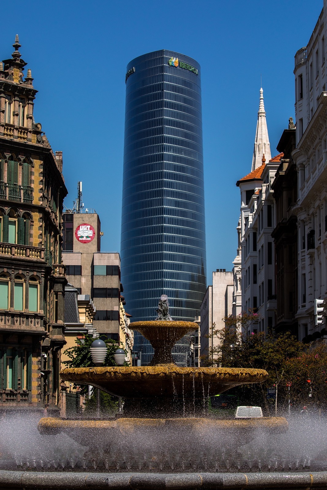 毕尔巴鄂市中心的莫尤亚广场是为了纪念本市1909-1913&1924-1930的双任期市长费德里科-莫尤亚(Federico Moyua)而建立的,建筑师何塞-路易斯-萨利纳斯在1940年就将其规划为市中心枢纽的一部分,最终在60年后他的儿子曼努埃尔-萨利纳斯(Manuel Salinas)完成了这项城市改造工程,保留了中心的喷泉,以及法式花坛。周围围绕着有名的老建筑,而向西北望去就是正对伊贝尔德洛拉塔的轴线,这座建筑高165米,是西班牙北部区域的最高建筑,建筑师塞萨尔-佩里(Cesar Pelli),古老的喷泉搭配崭新的摩天大厦这个取景非常符合毕尔巴鄂这座城市给我的感觉,他新旧融合,并不突兀,甚至和谐,一个值得逗留欣赏的美丽城市应该有如此的魄力与内涵~ok,记下来我们继续前进。